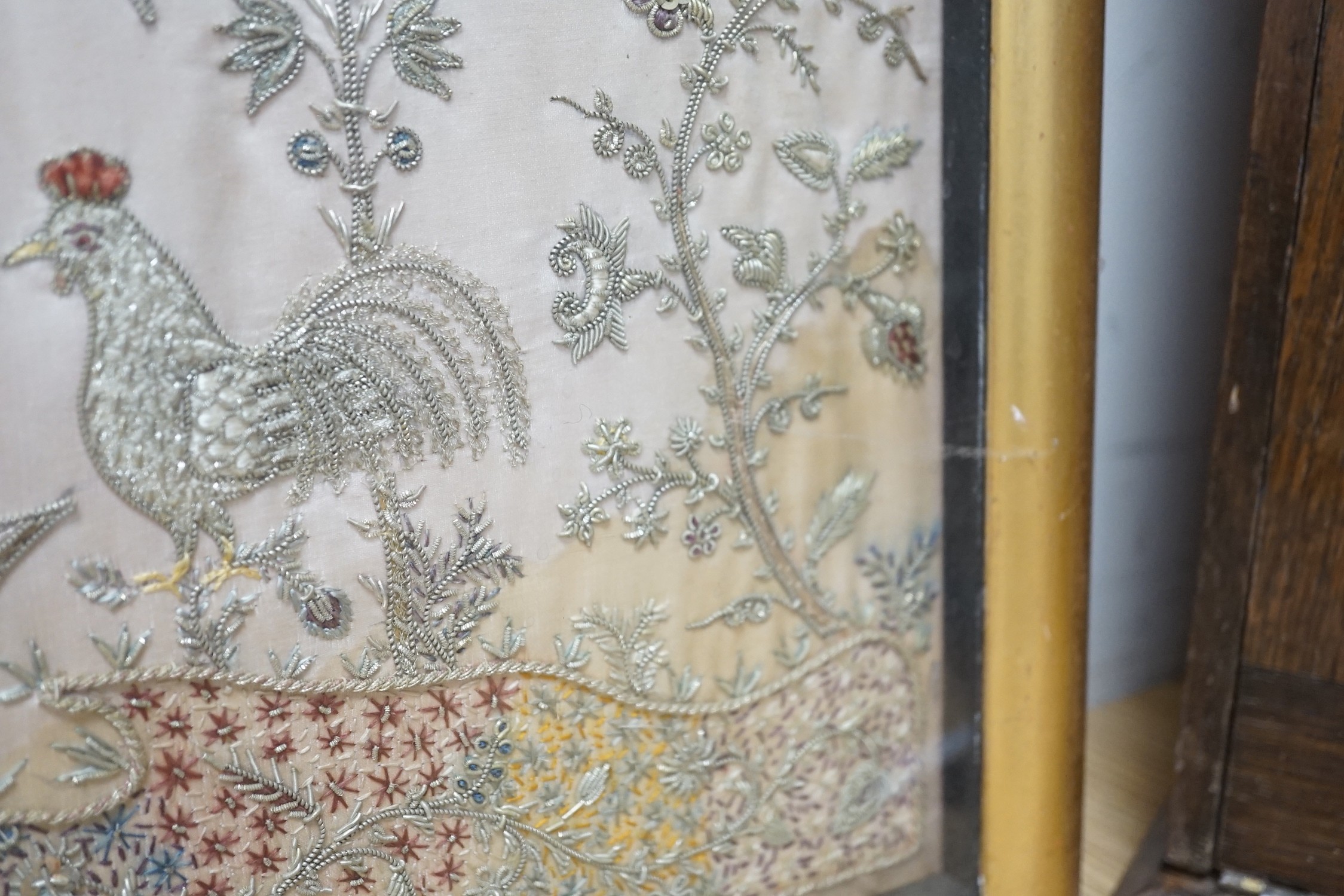 A framed silk, multi coloured metal thread embroidered Indian panel: a peacock seated amongst birds, flowers and leaves in a tree, 110cms x 51cms
